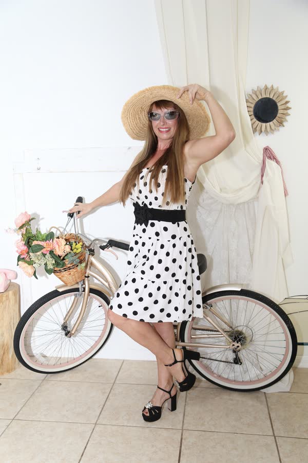 Woman in polka-dot dress posing with a vintage bicycle at a themed photo event