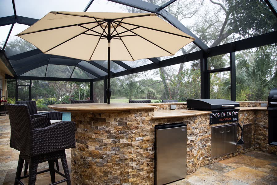 Outdoor kitchen with stone bar seating under a screened Florida lanai
