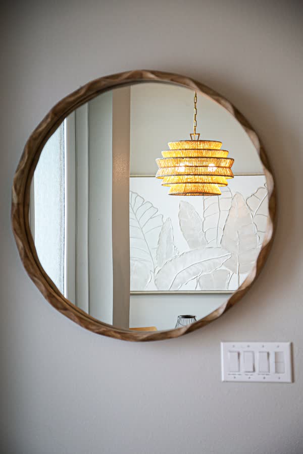 Round carved wood mirror reflecting a pendant light fixture
