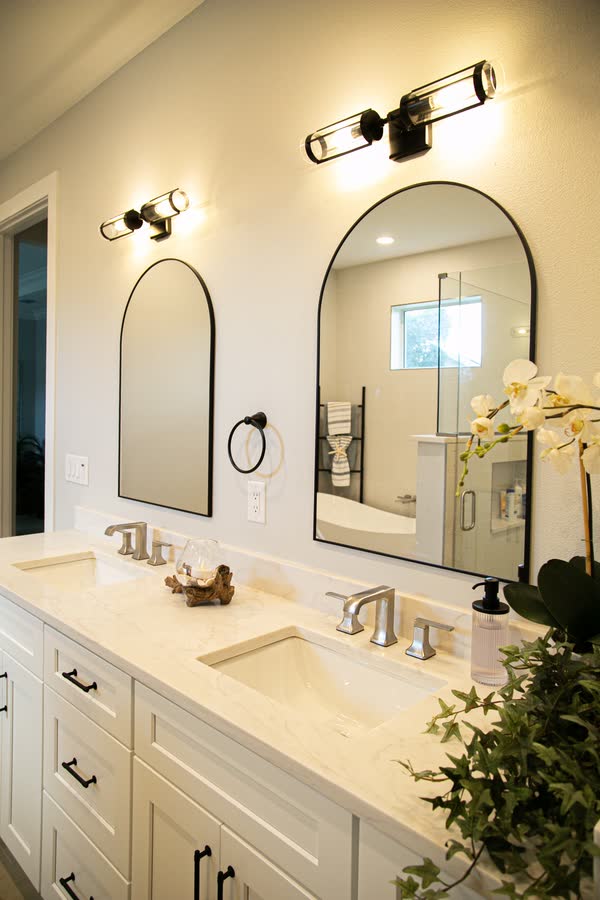Primary bathroom double vanity with arched mirrors and sconce lighting